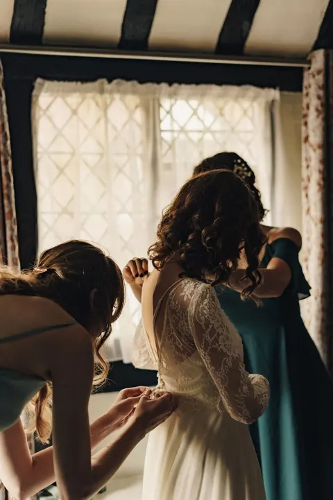 Bride having her dress adjusted beside a leaded window