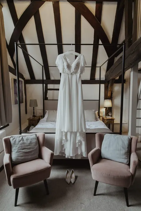 Wedding dress hanging between exposed beams above two armchairs